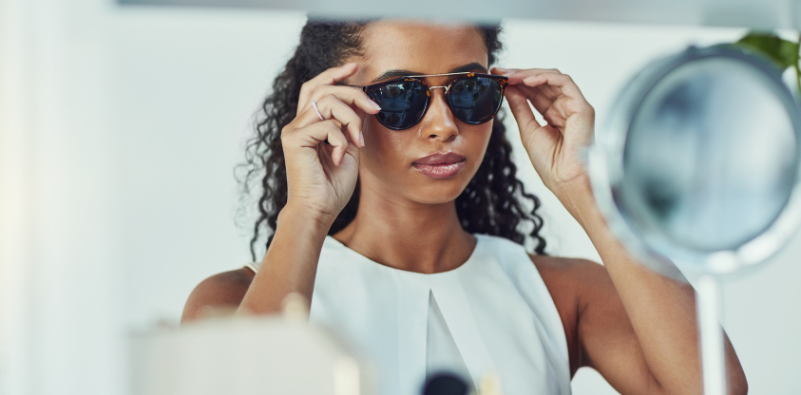 A woman at the eye doctor's office trying on a pair of sunglasses in front of a mirror.